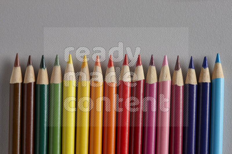 A collection of colored pencils arranged showcasing a gradient of different hues on grey background