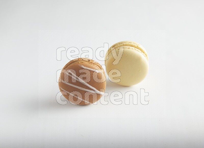 45º Shot of of two assorted Brown Irish Cream, and Yellow Vanilla macarons on white background
