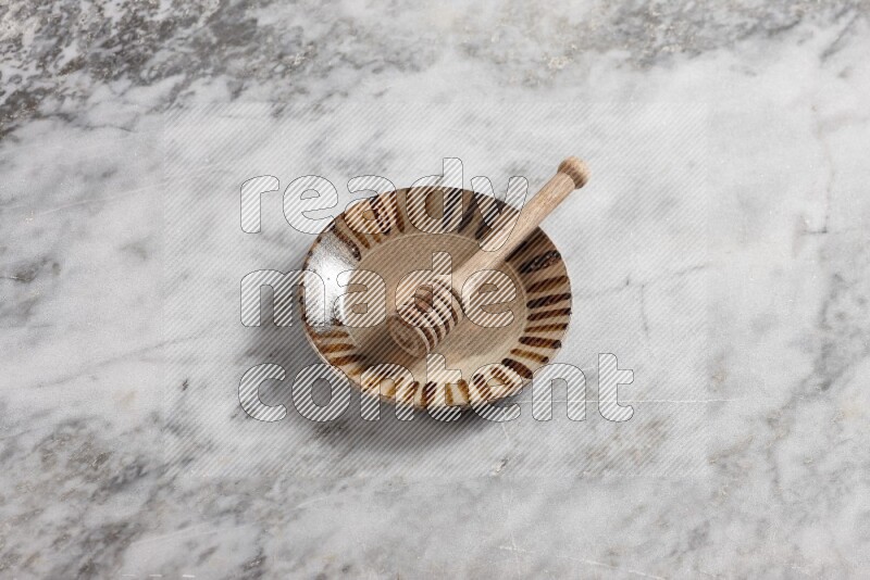 Multicolored pottery plate with wooden honey dipper in it on grey marble background