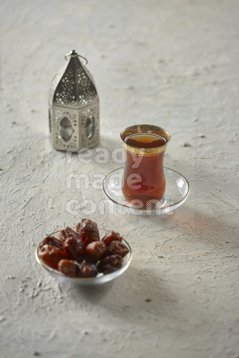 A silver lantern with different drinks, dates, nuts, prayer beads and quran on textured white background