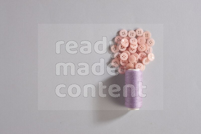 بكرة خيط خياطة أرجوانية مع مجموعة صغيرة من الأزرار على خلفية رمادية