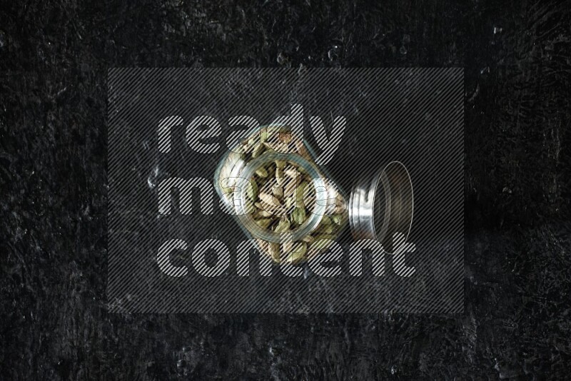 وعاء بهارات زجاجي ممتلئ بحبوب الهيل على خلفية سوداء