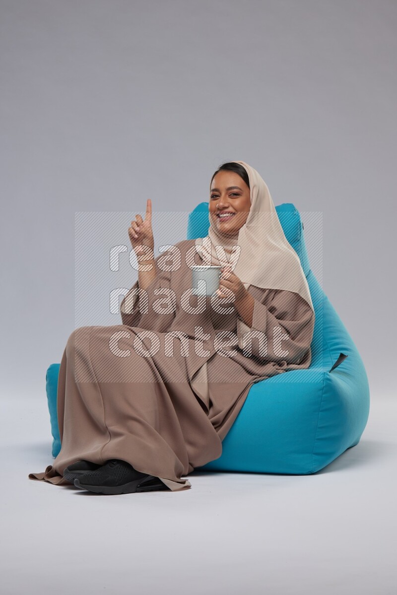 A Saudi woman sitting on a blue beanbag and drinking coffee