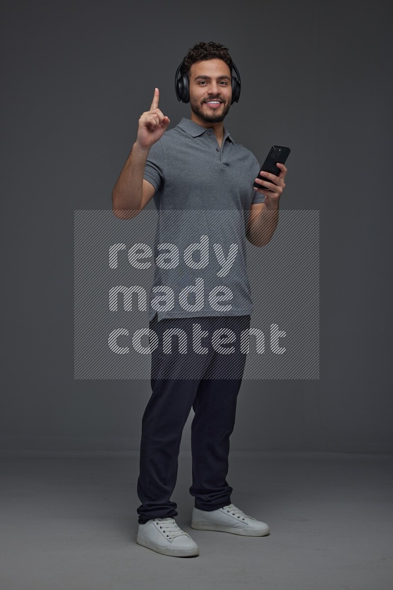A man wearing casual and using his phone and headphone eye level on a gray background