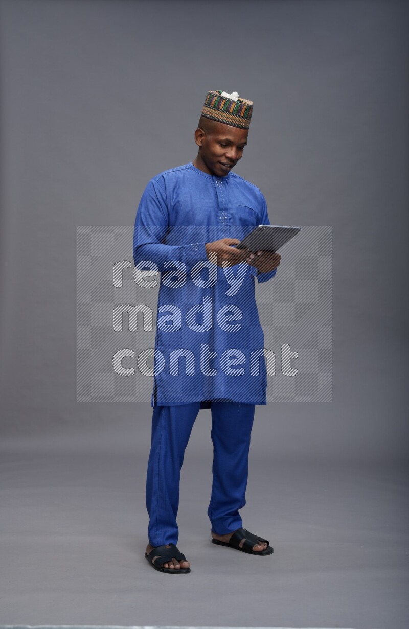 Man wearing Nigerian outfit standing working on tablet on gray background