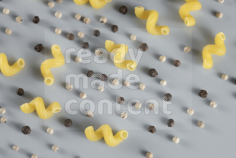 Raw pasta with different ingredients such as cherry tomatoes, garlic, onions, red chilis, black pepper, white pepper, bay laurel leaves, rosemary, cardamom and mushrooms on light blue background