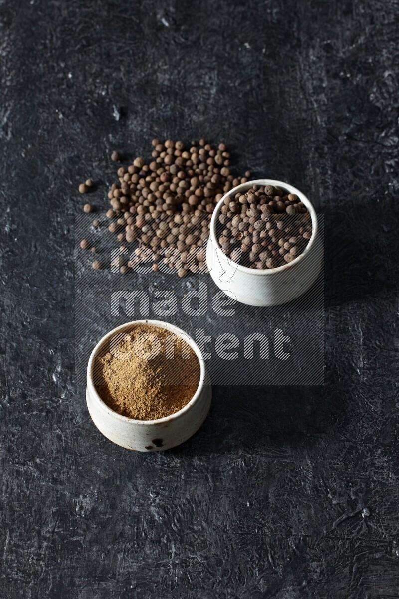 وعاءان بيج، أحدهما ممتلئ ببودرة بهار الفلفل الحلو والآخر بالحبوب وكلاهما متناثران على خلفية سوداء