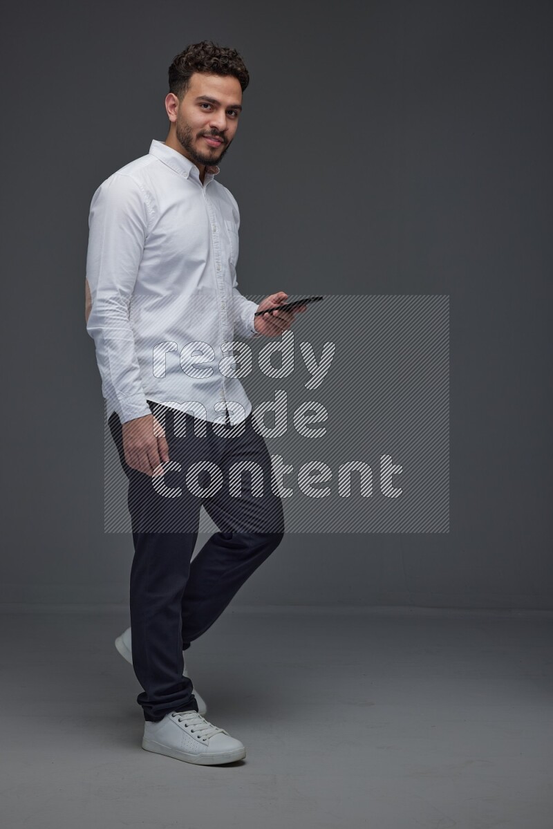 A man wearing smart casual standing and using his phone eye level on a gray background