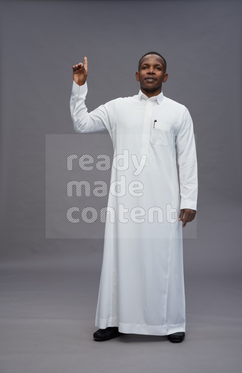 Saudi man wearing thob standing interacting with the camera on gray background