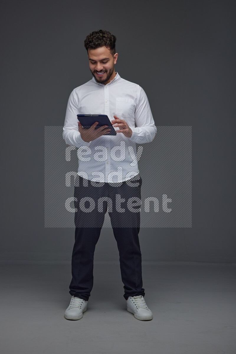A man wearing smart casual standing and using his tablet eye level on a gray background