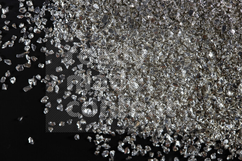 Silver shimmering fragments of glass scattered on a black background