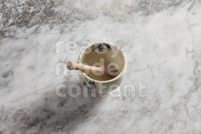 Decorative pottery bowl with wooden honey dipper in it on grey marble background