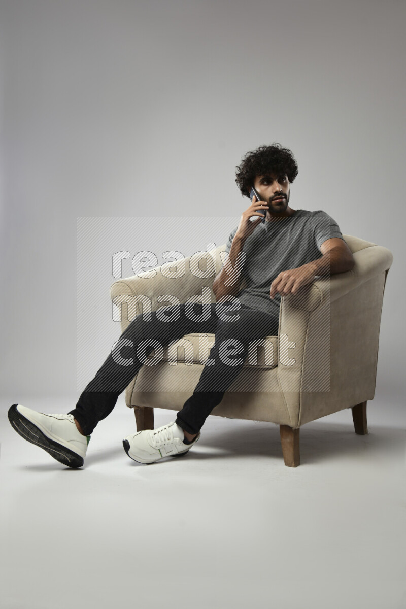 A man wearing casual sitting on a chair talking on the phone on white background