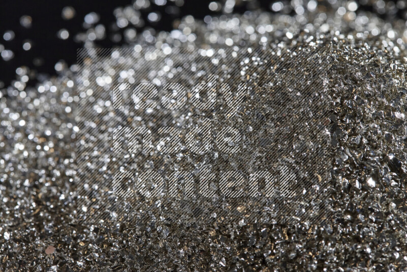Silver shimmering fragments of glass scattered on a black background