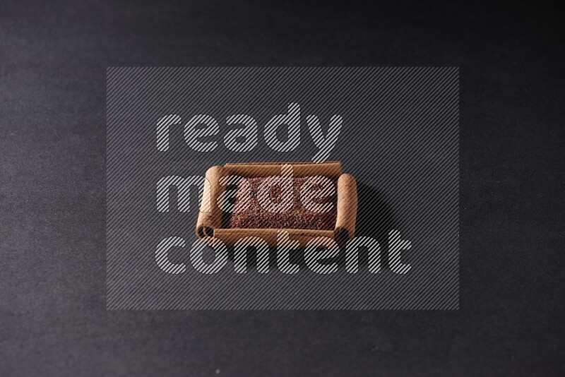 A single square of cinnamon sticks full of garden cress on black flooring