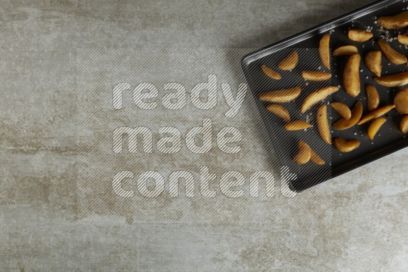 wedges potato in a black stainless steel rectangle tray on grey textured counter top