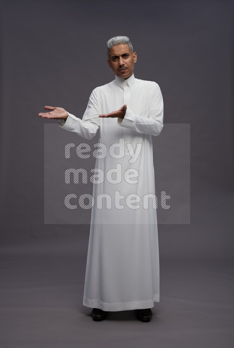 Saudi man wearing thob standing interacting with the camera on gray background