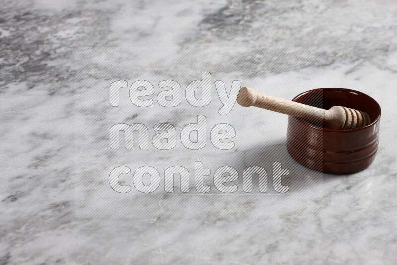Brown pottery bowl with wooden honey dipper in it on grey marble background