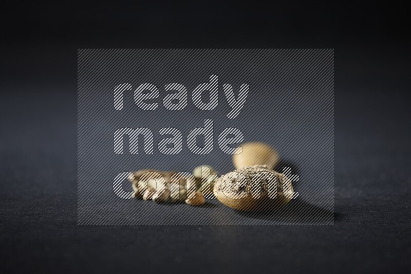 A wooden spoon full of cardamom powder and cardamom seeds beside it on black flooring