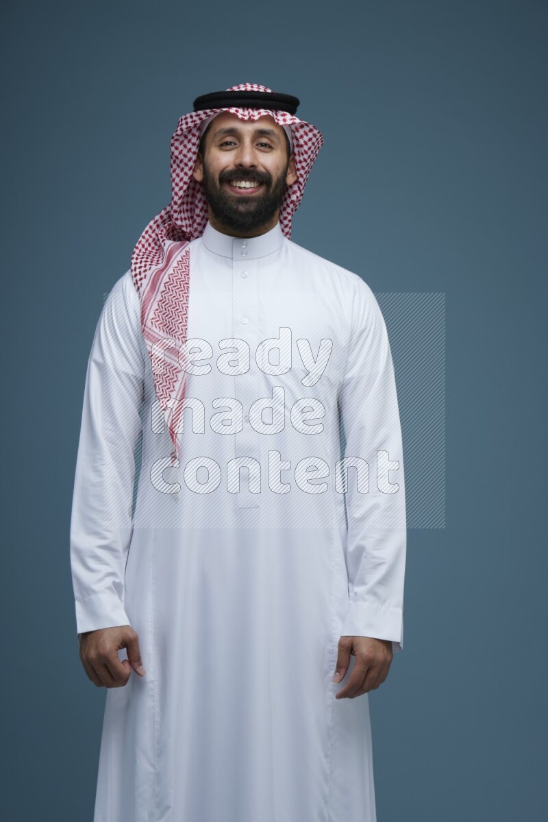 A man posing in a blue background wearing Saudi Thob and Shomag