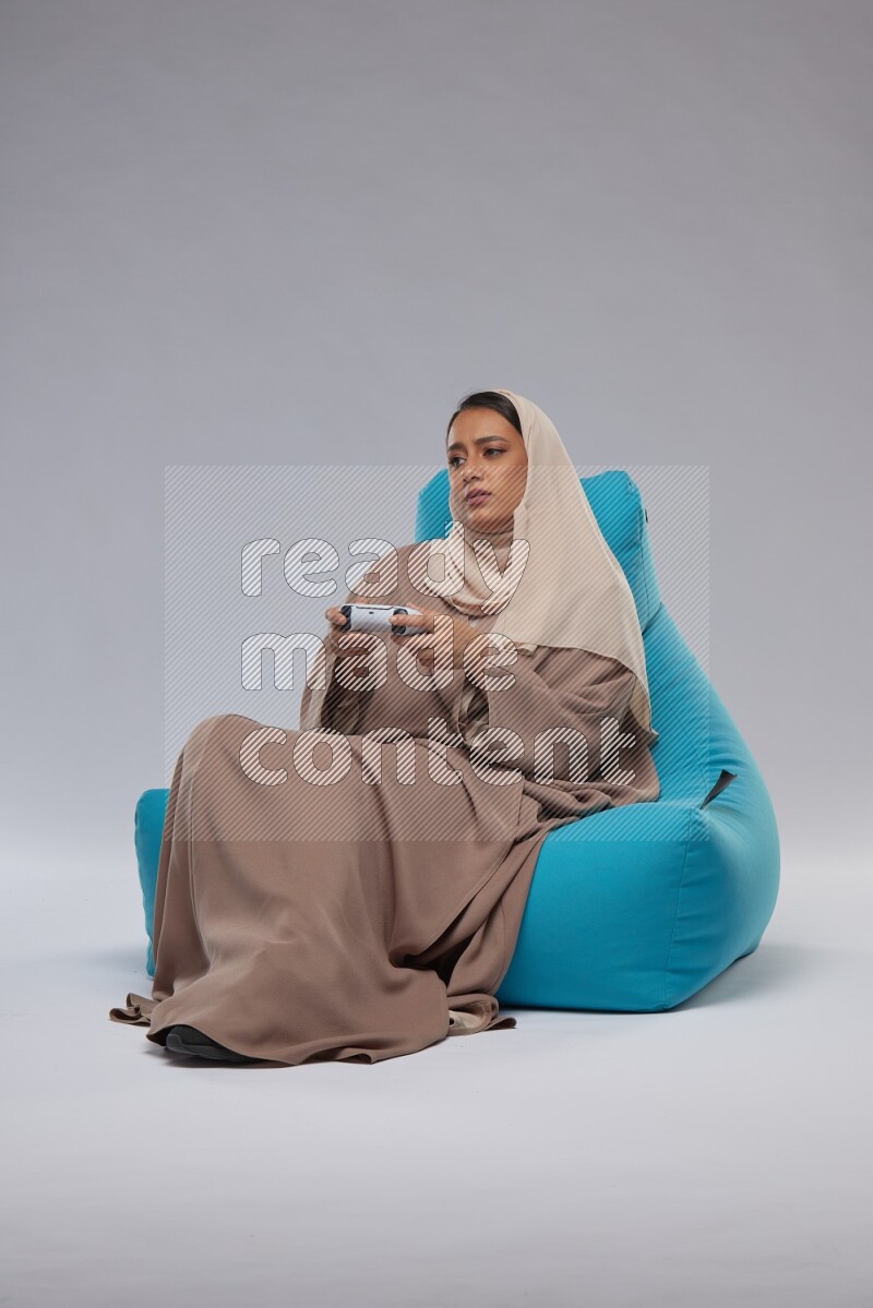A Saudi woman sitting on a blue beanbag and gaming with joystick
