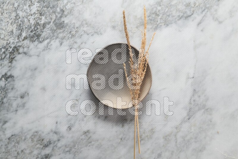 Wheat stalks on multicolored pottery plate on grey marble background