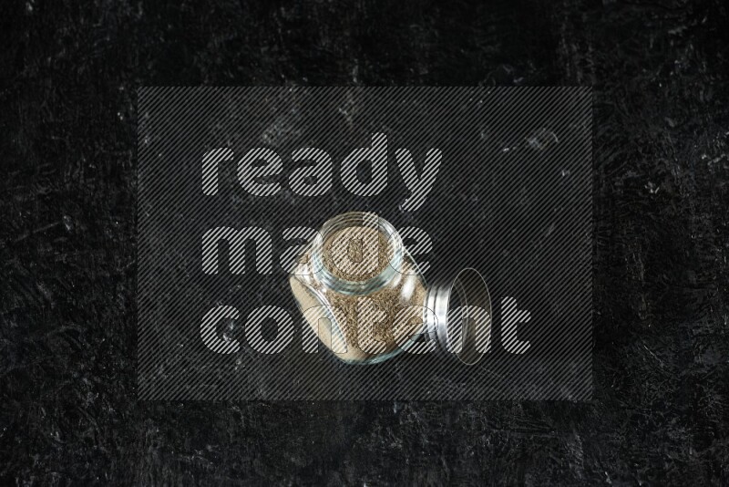 وعاء زجاجي للتوابل ممتلئ ببودرة الهيل على خلفية سوداء