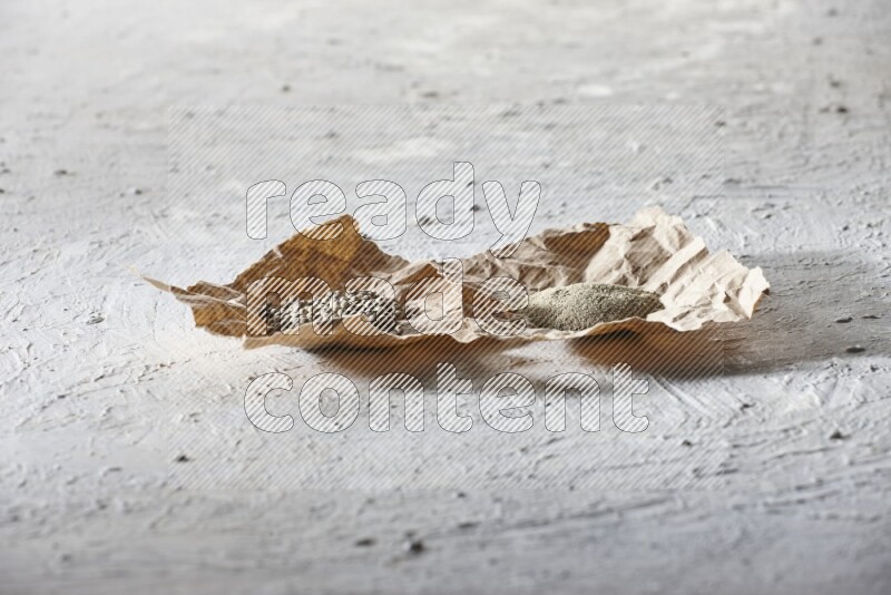 White pepper beads and powder in crumpled pieces of paper on textured white flooring