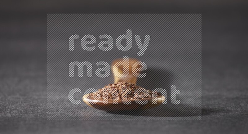 A wooden ladle full of flaxseeds on a black flooring