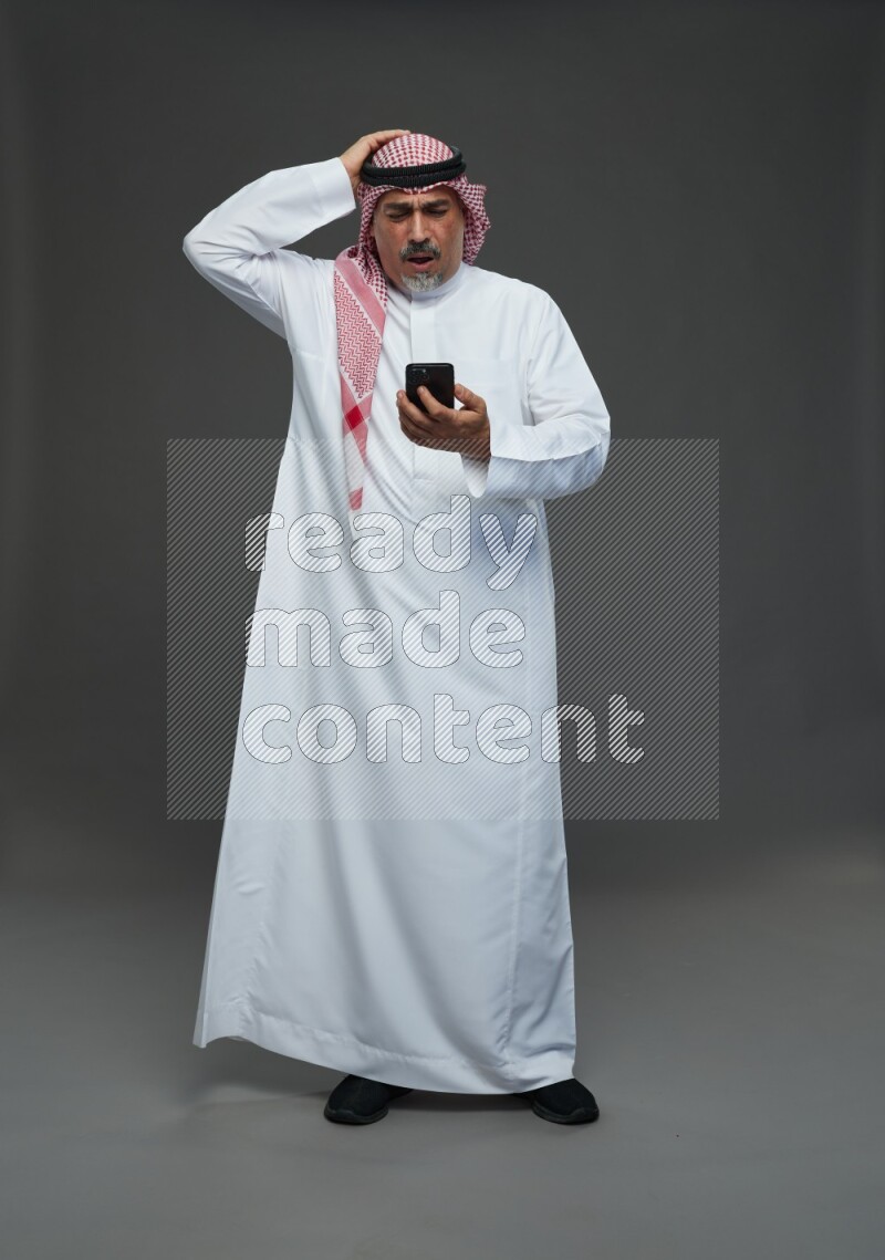 Saudi man with shomag Standing texting on phone on gray background