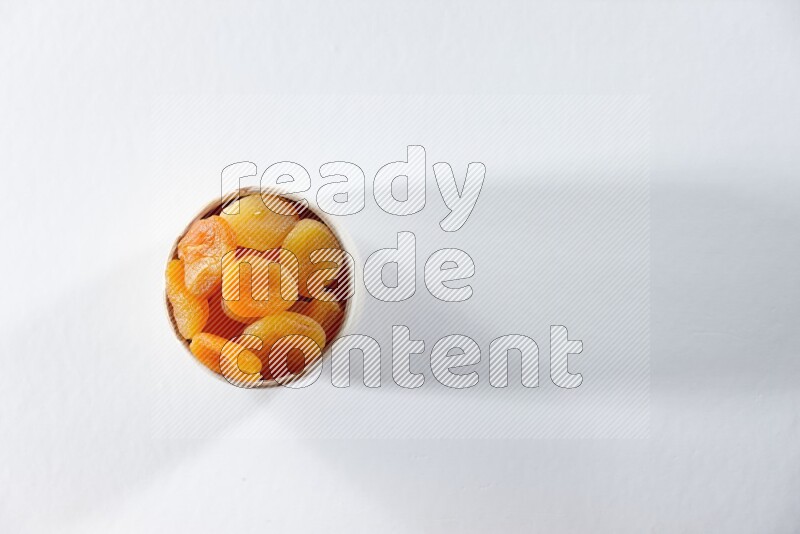 A beige ceramic bowl full of dried apricots on a white background in different angles