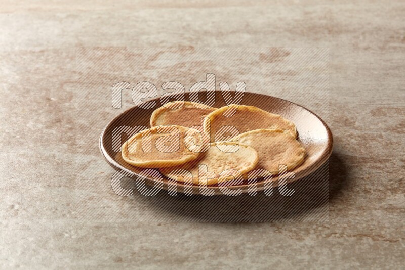Five stacked plain mini pancakes in a brown plate on beige background