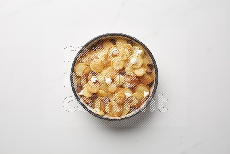 Top-view shot of mixed chocolate chips cereal pancakes in a round bowl on white background