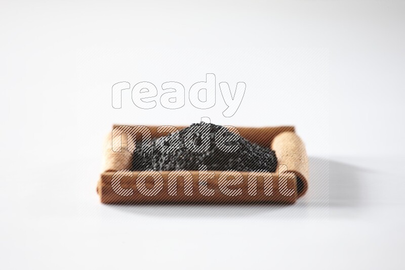 أربعة من أعواد القرفة مكونة شكل مربع بداخلها حبة البركة علي خلفية بيضاء