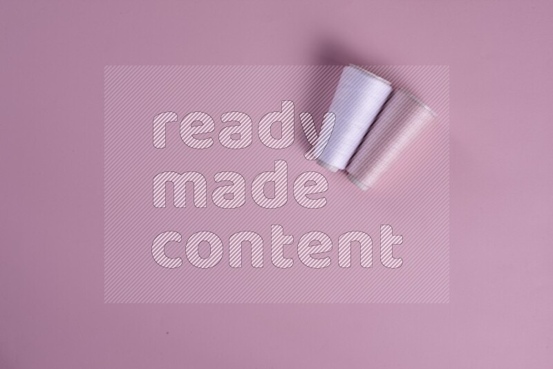 A white and pink collection of sewing and tailoring tools arranged on a pink background