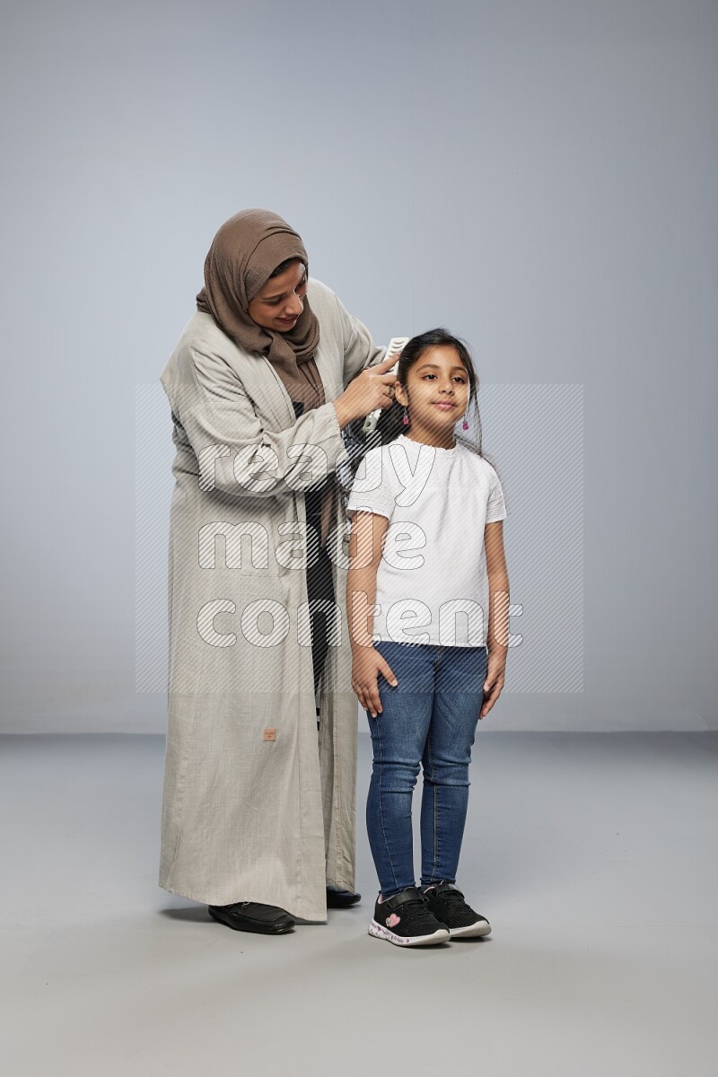 Mom standing styling hair for her daughter on gray background