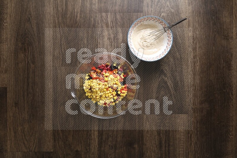 A bowl full of salad (avocado, tomatoes, red beans, olives, bell pepper, corn, lettuce) and bowl of salad dressing on wooden background
