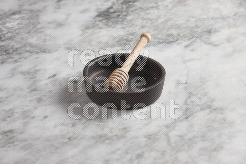 Black pottery oven plate with wooden honey dipper in it on grey marble background