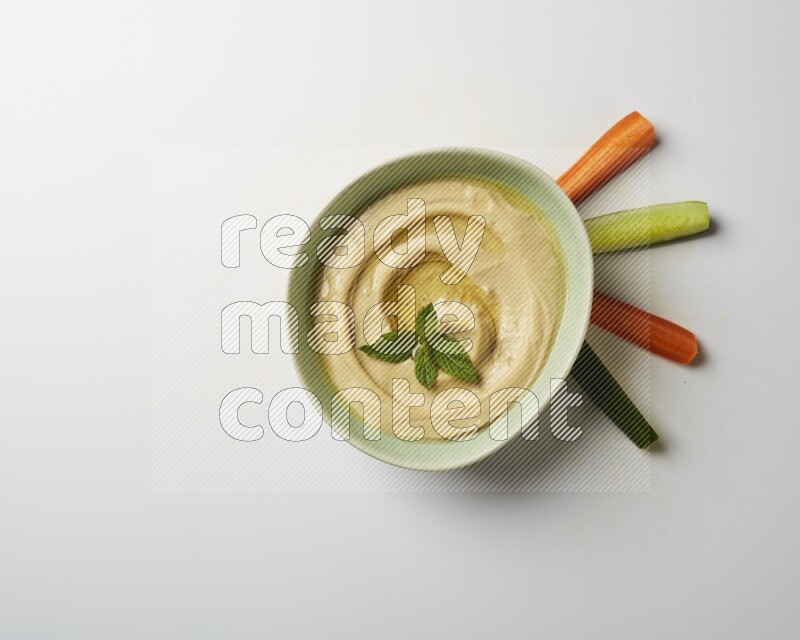 Hummus in a green plate garnished with mint on a white background