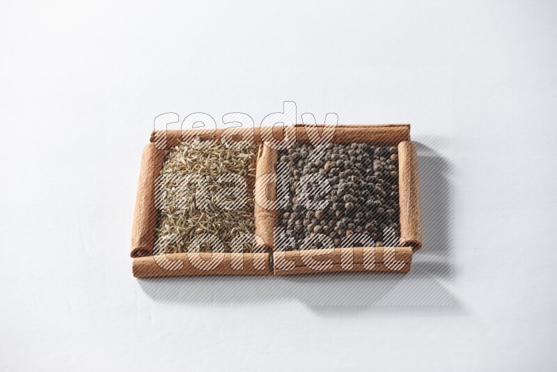 مربعان من أعواد القرفة ممتلئان بحبوب الفلفل الأسود وحبوب الكمون علي خلفية بيضاء