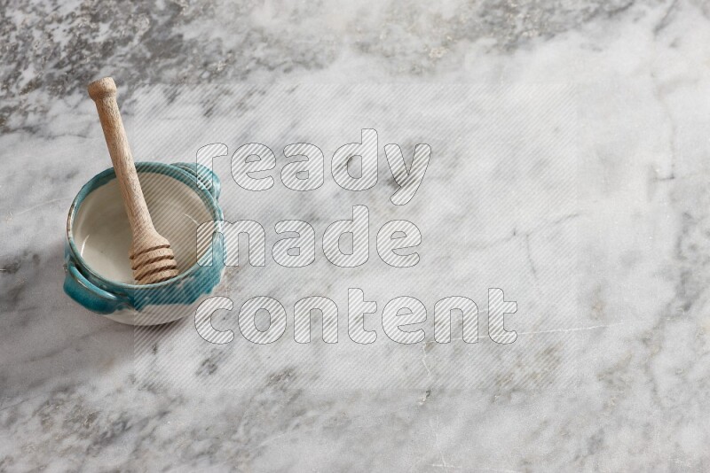 Multicolored pottery bowl with wooden honey dipper in it on grey marble background