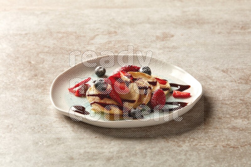 Five stacked mixed berries mini pancakes in a bicolor plate on beige background
