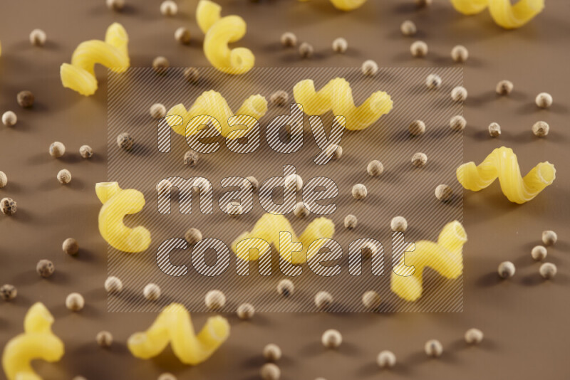 Raw pasta with different ingredients such as cherry tomatoes, garlic, onions, red chilis, black pepper, white pepper, bay laurel leaves, rosemary and cardamom on beige background