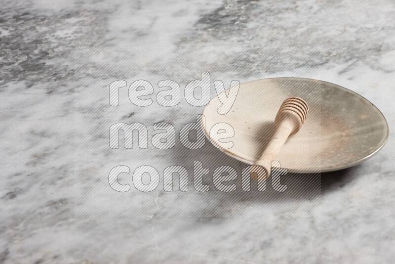 Multicolored pottery plate with wooden honey dipper in it on grey marble background