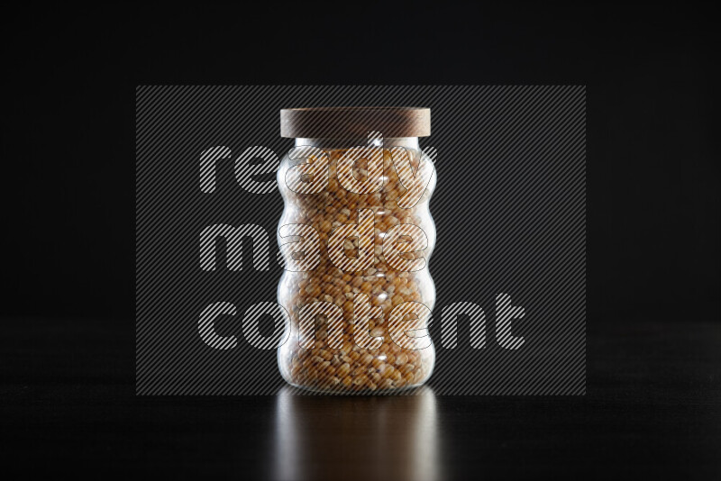 Dry corn kernels in a glass jar on black background