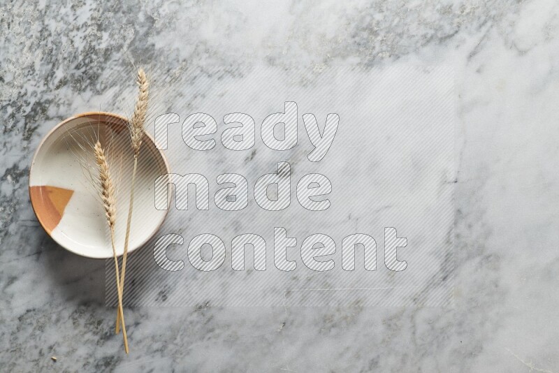 Wheat stalks on multicolored pottery plate on grey marble background