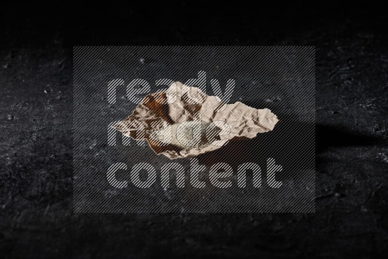 White pepper powder in a crumpled paper on textured black flooring