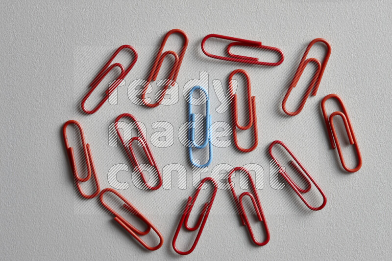 A bunch of red paper clips with a different colored paper clip in the center on grey background