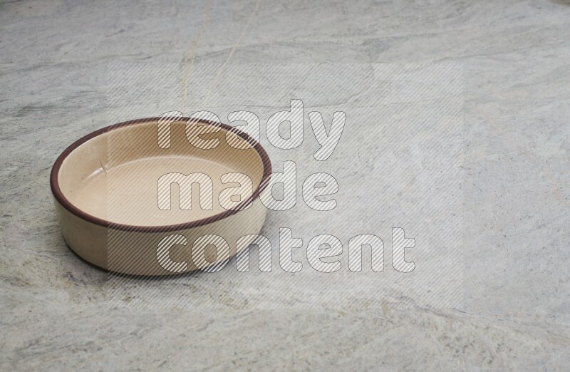 A beige pottery oven bowl on grey marble background
