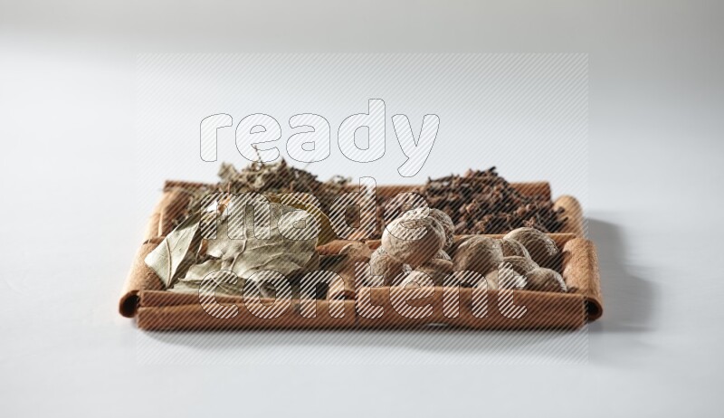 4 squares of cinnamon sticks full of bay laurel leaves, dried basil, cloves and nutmegs on white flooring